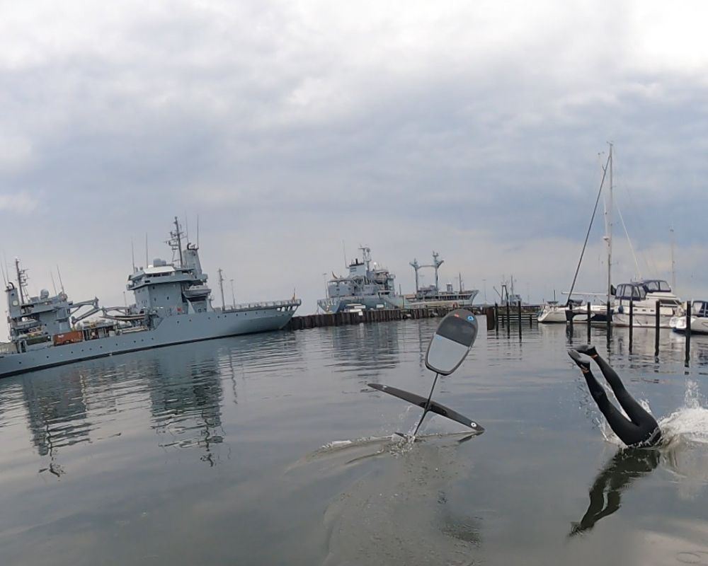 A chair partially submerged in water near ships and a cloudy sky.