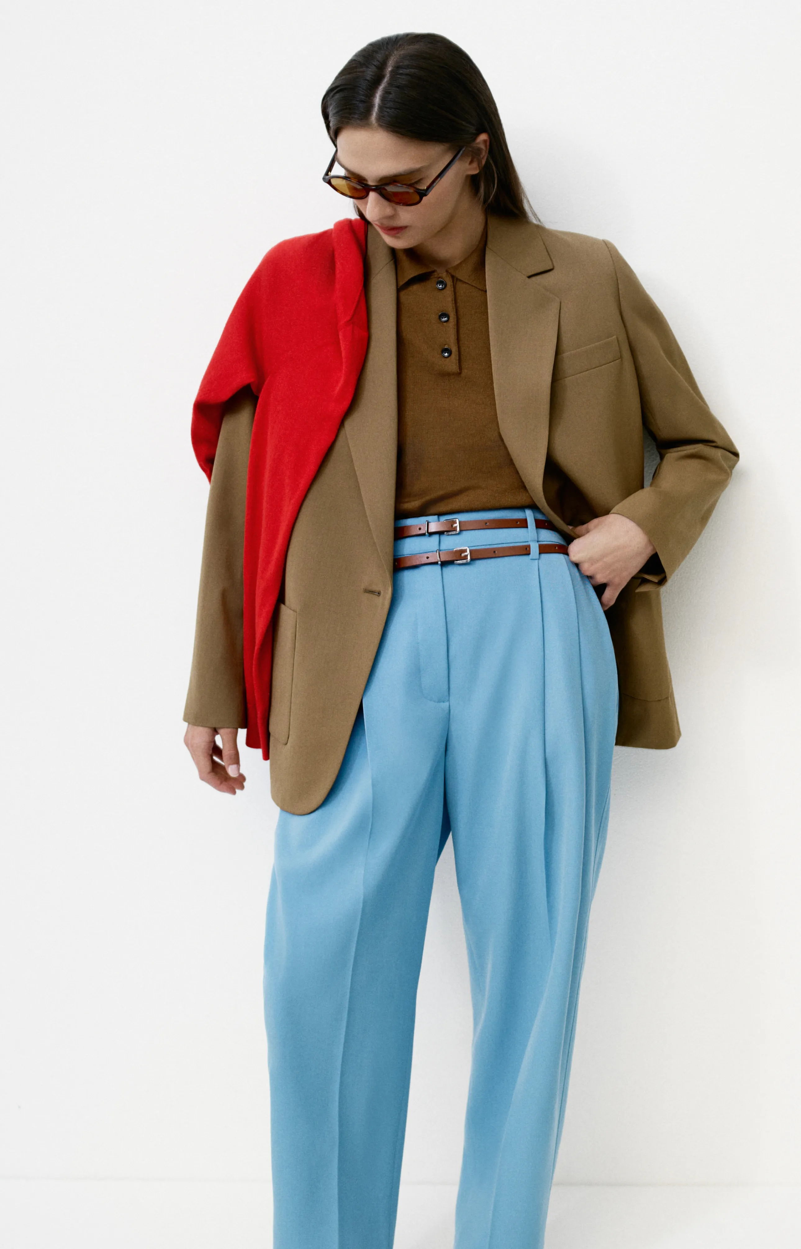Person wearing a brown blazer, blue trousers, and a red sweater.