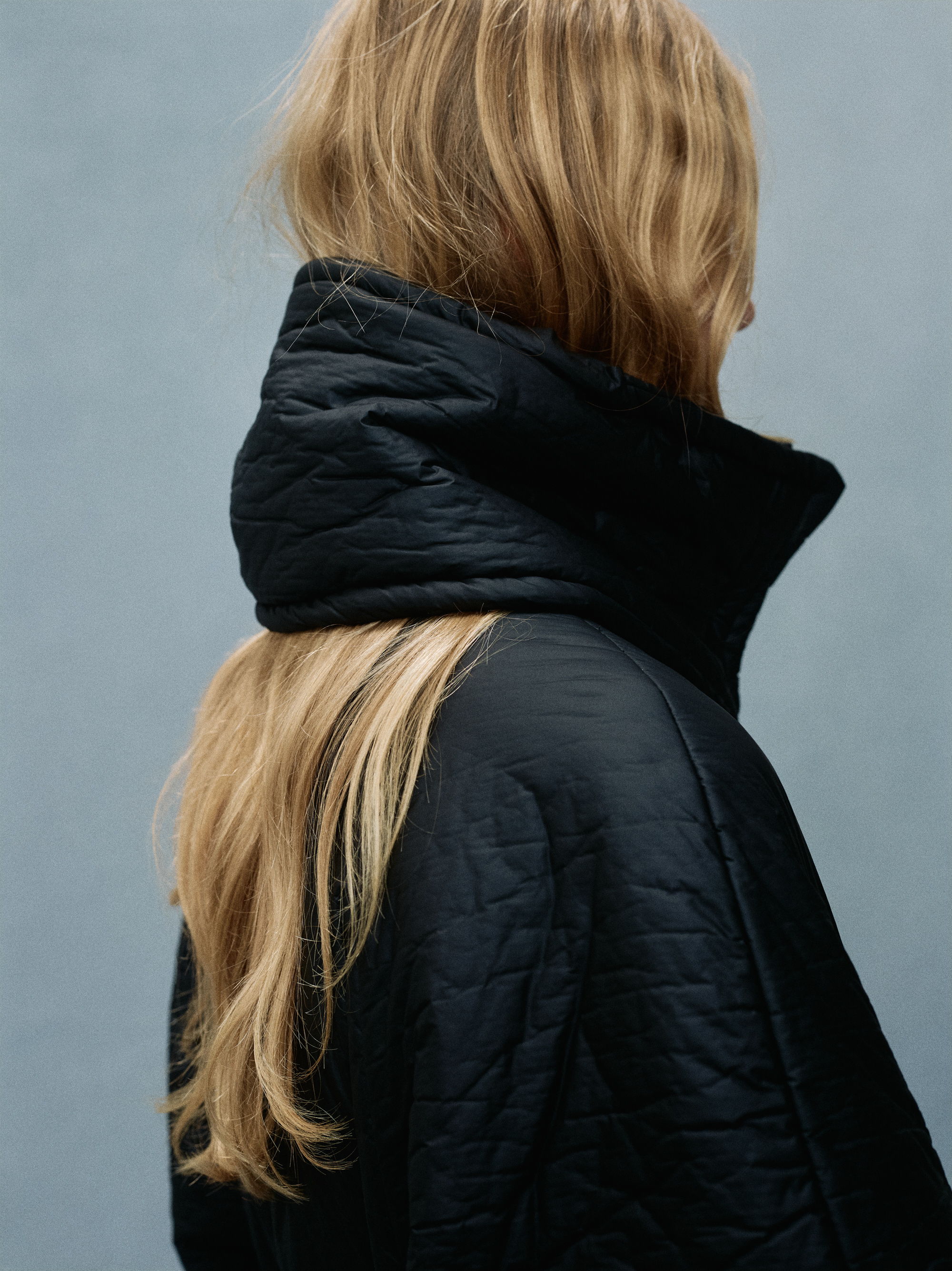 Person with long hair wearing a black coat, viewed from the back.