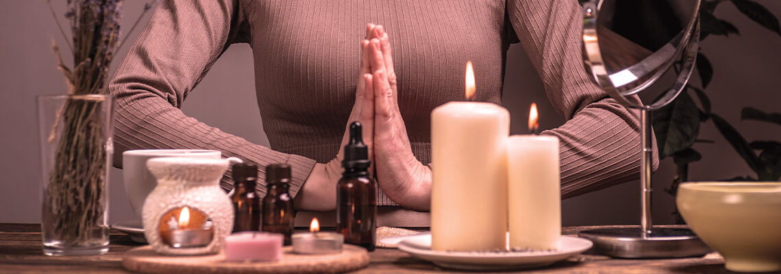 A person with hands in prayer position beside candles and wellness products.