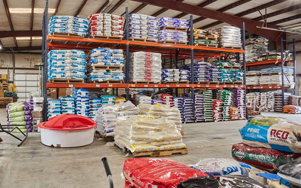 Warehouse interior with stacked bags on shelves and various products on the floor.