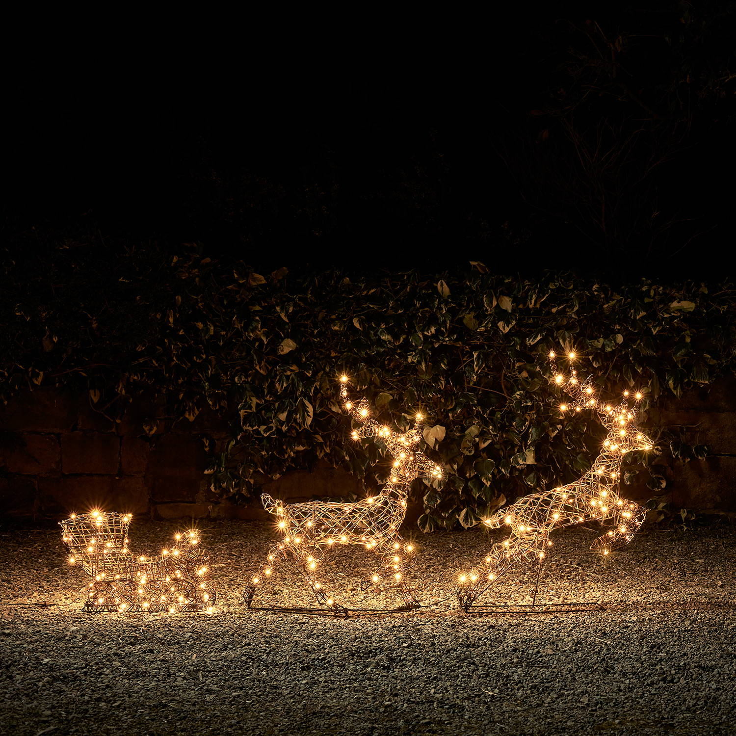 Warm white LED lit reindeer and sleigh in a dark garden setting