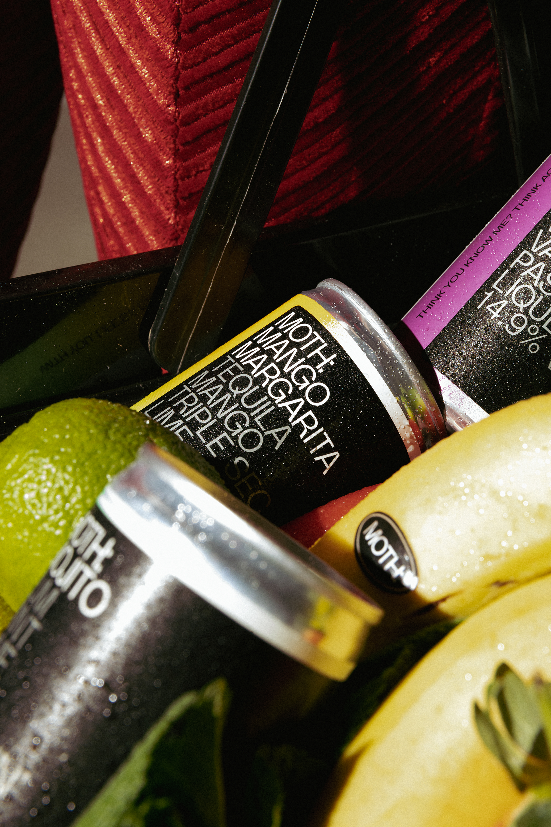 Cans of margarita cocktail among sliced fruit on a table.