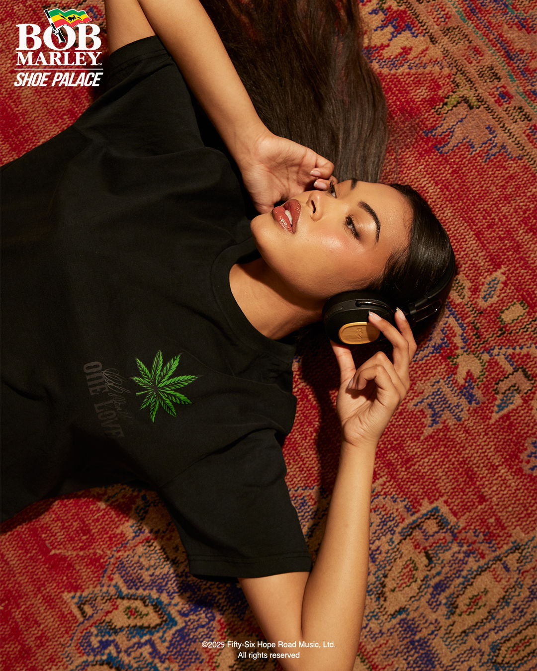 Young woman in black shirt wearing headphones, lying on patterned rug.
