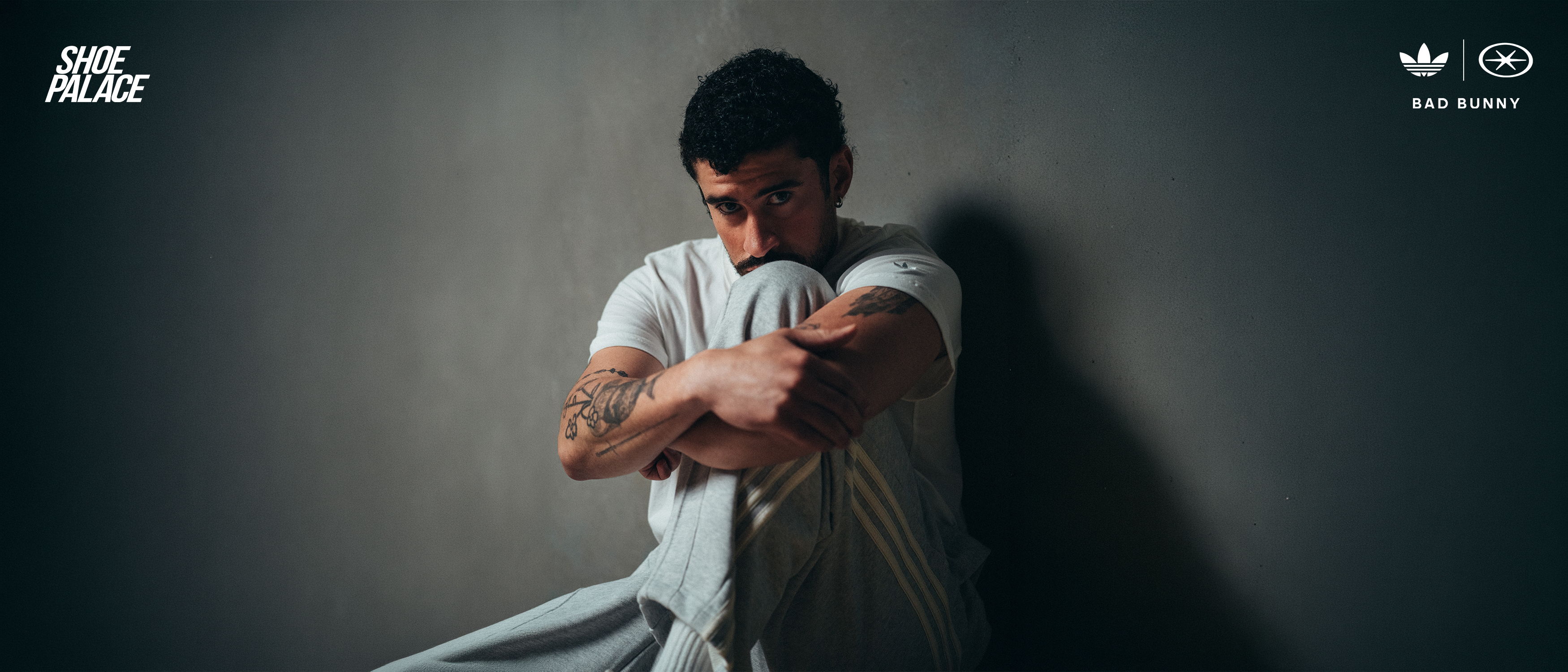Person sitting against a wall, hugging knees, in a contemplative pose.