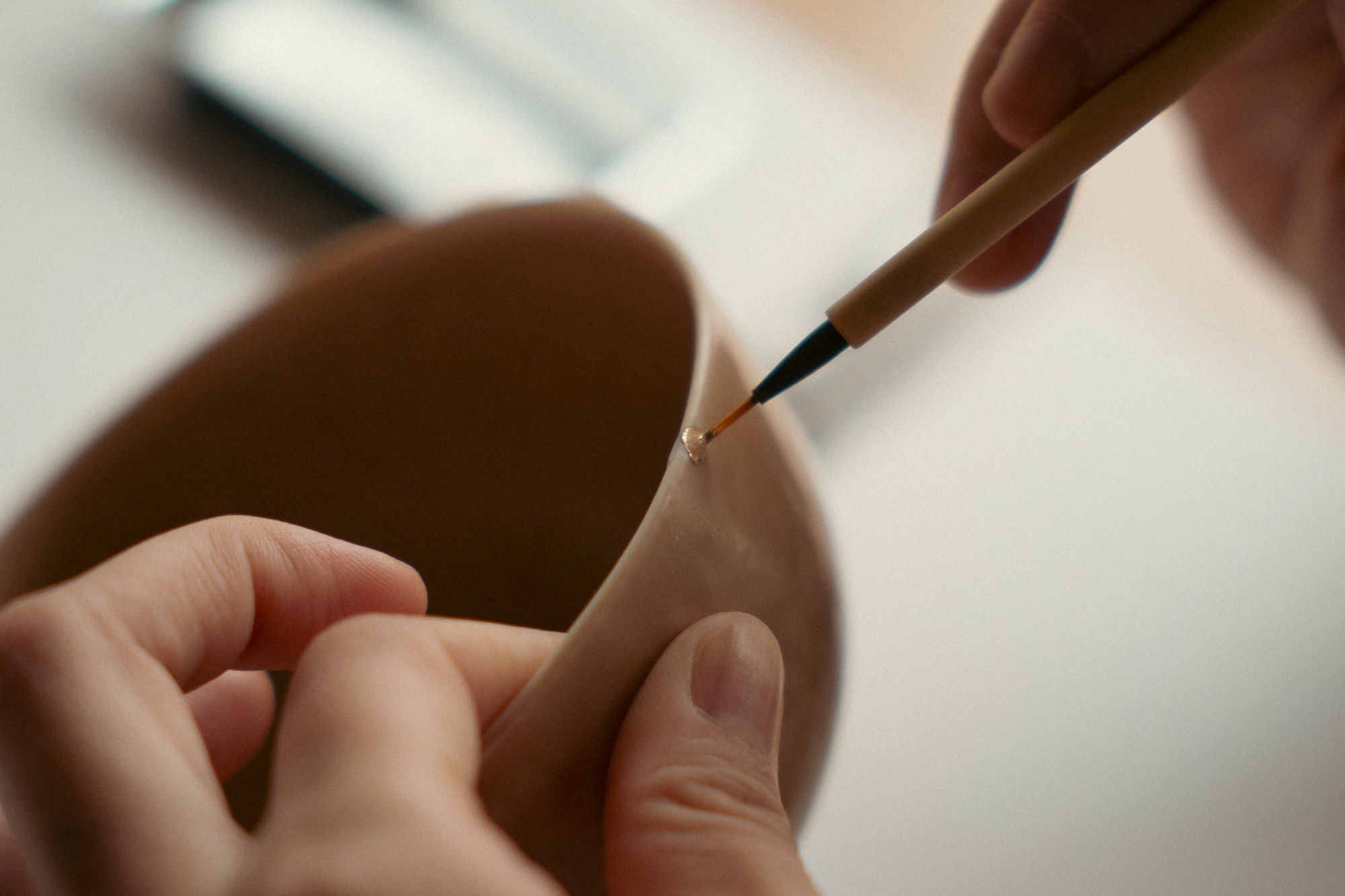 A person painting a clay pot with a small brush.