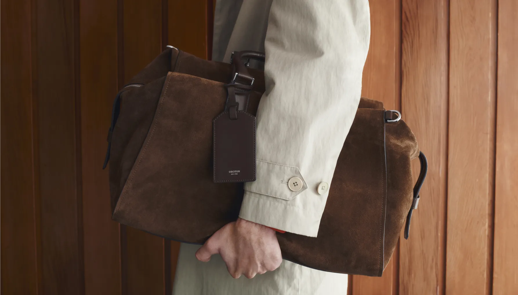 Person holding a brown suede bag against a wooden background.