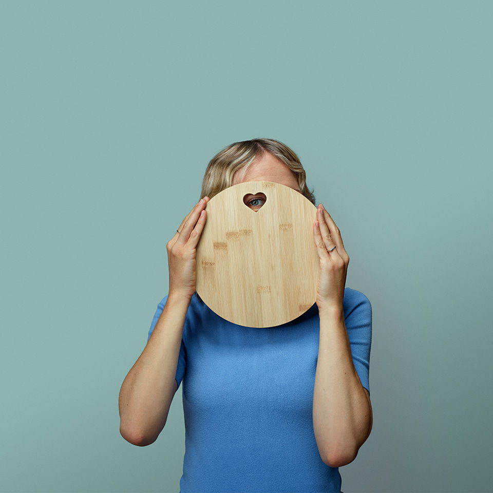 Person holding a round wooden board in front of their face.