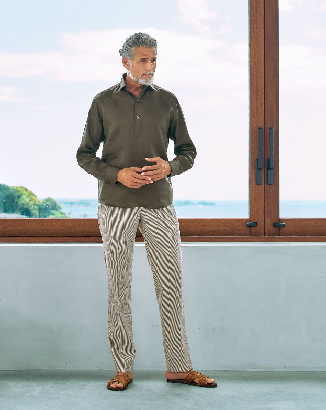 Man standing by a window, wearing a casual outfit with a scenic view.