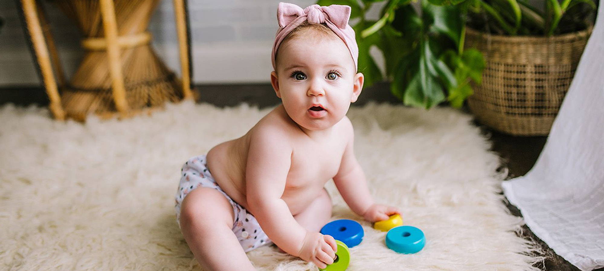 Cozy baby sitting on the rug looking like cute and surprised in his pair of Simple Being reusable cloth diapers. Simply Comfortable. 