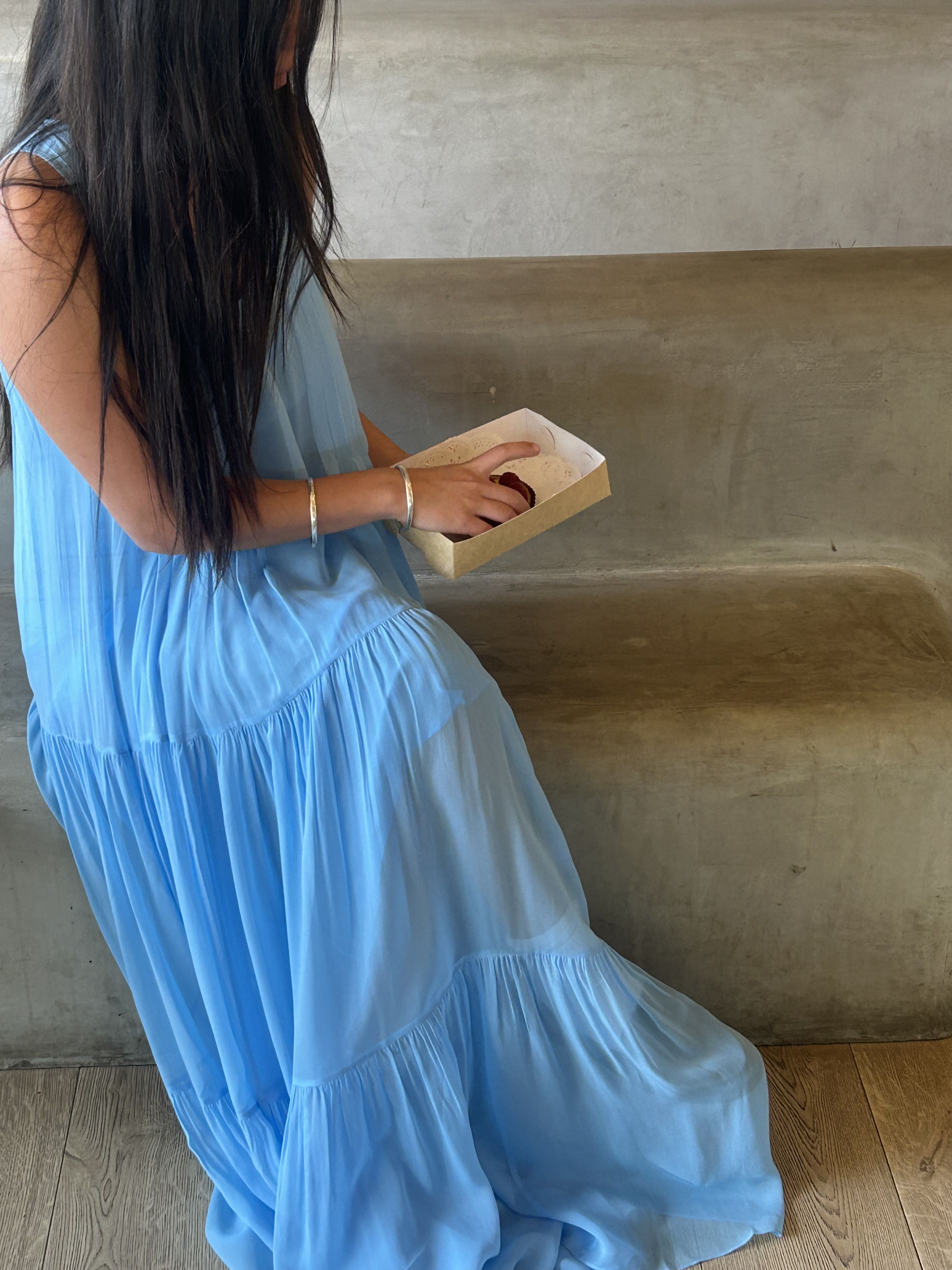 Frankie sits in Labannette with a pastry. She is wearing the Jena Cami Dress in Sky.