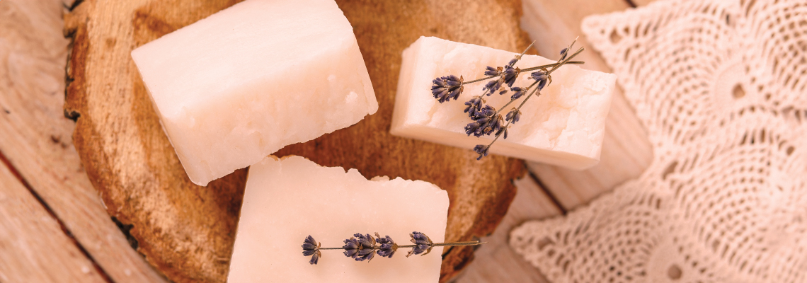 Three handmade soap bars on a wooden surface with lace.