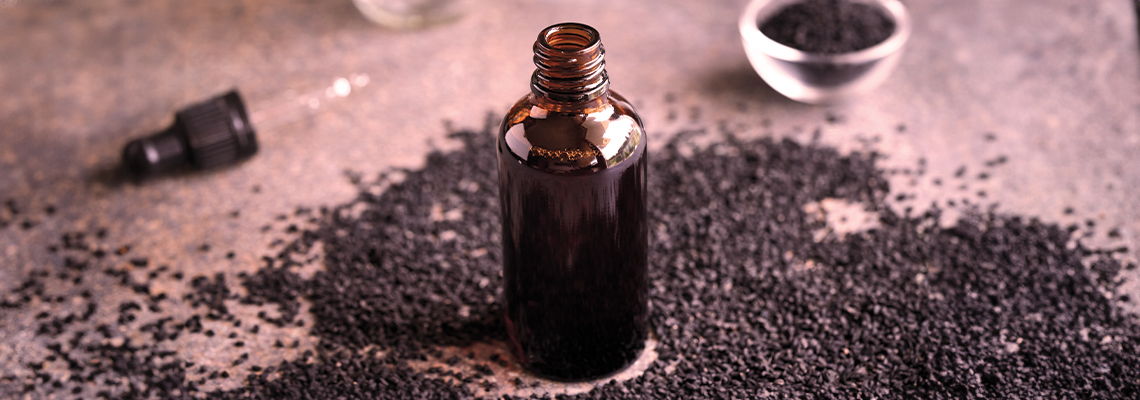 Glass bottle surrounded by black seeds on a textured surface.
