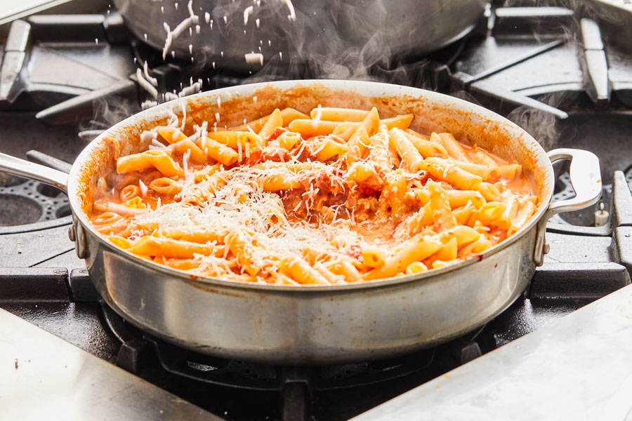 Penne pasta in a pot on the stove with a creamy red sauce and topped with grated cheese