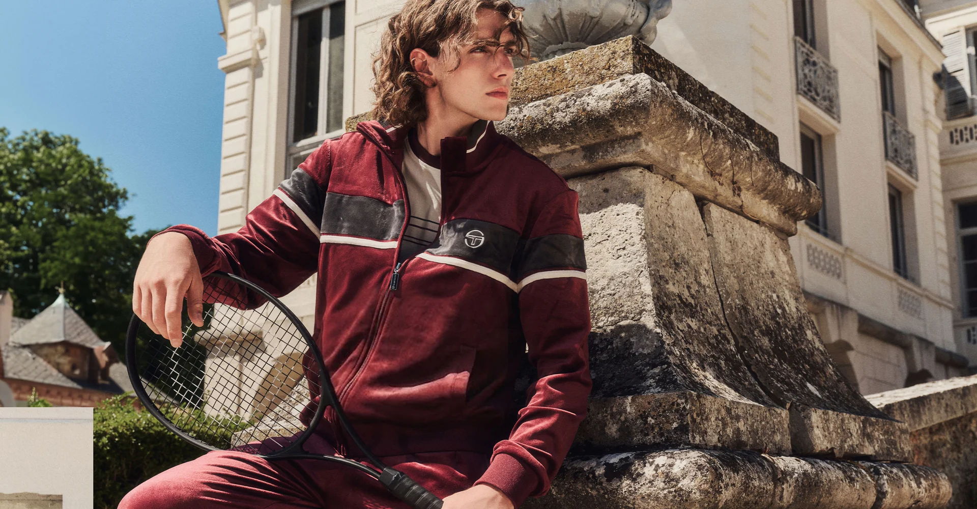Young person in maroon Sergio Tacchini athletic wear sitting on a stone wall.