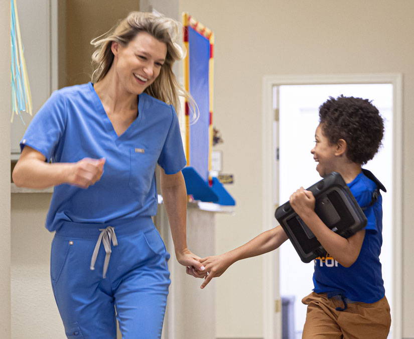 Young boy running with his SLP, holding a Tobii Dynavox TD I-110 speech generating device