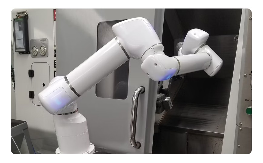 Robotic arm interacting with a machine in a workshop setting.