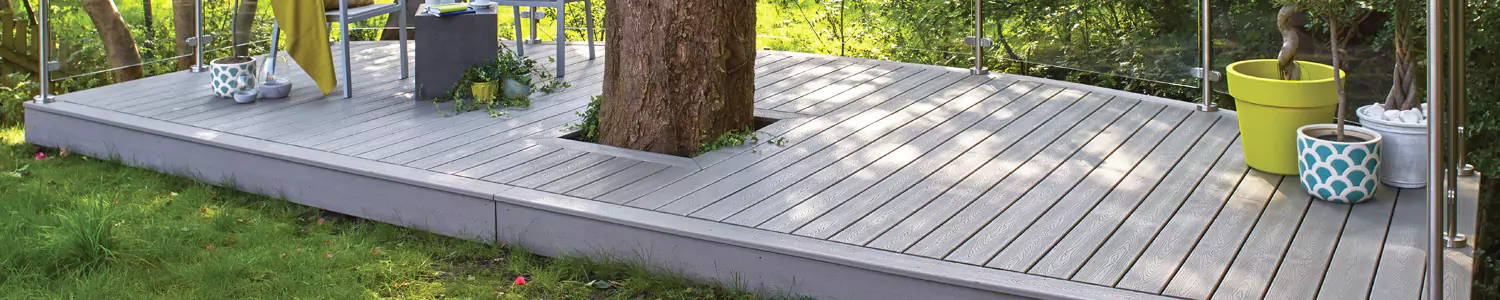 Composite decking installed in an outside garden and around a tree trunk, with platted pots and outdoor furniture placed on top of it. 