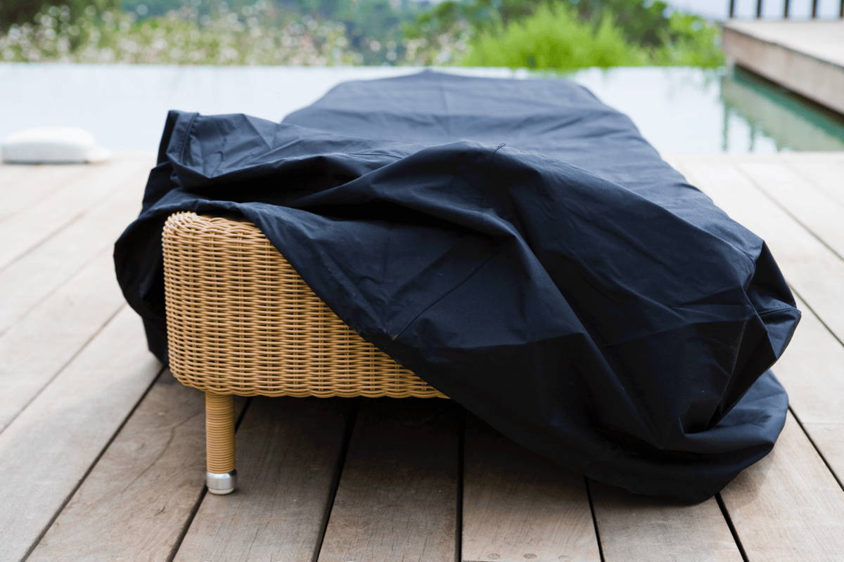An outdoor chaise lounger covered with a black cover. 