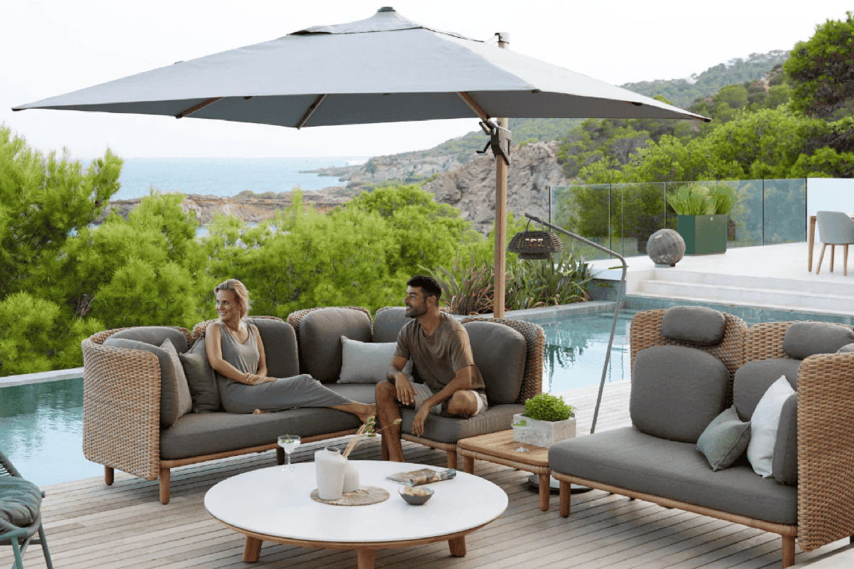 Poolside outdoor lounge with modern woven furniture and a large cantilever umbrella for shaded seating.