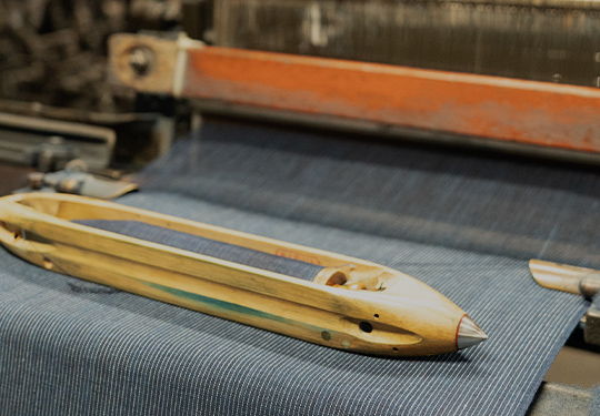 A shuttle on a weaving loom with blue fabric.