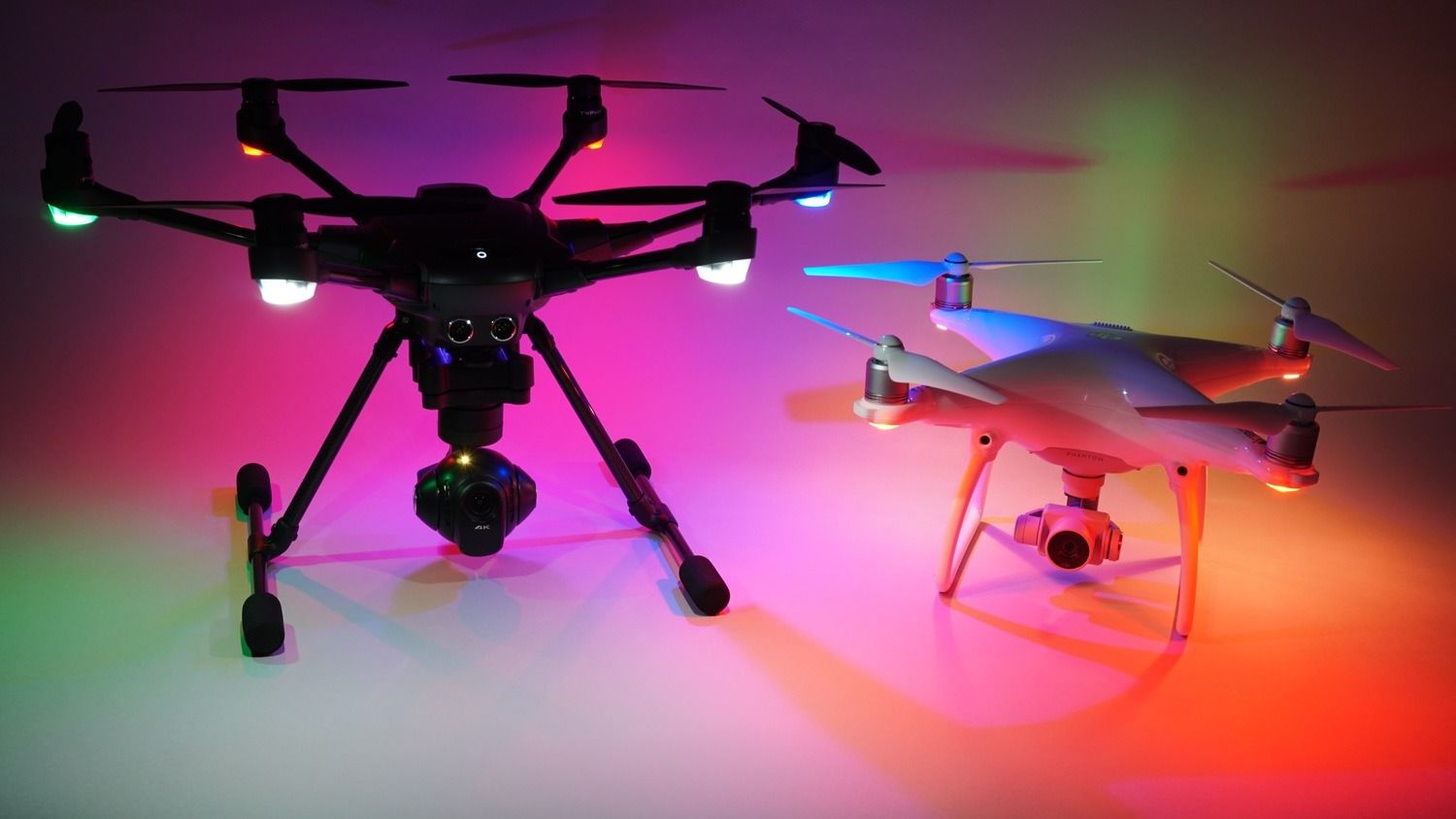 A Typhoon H and Phantom 4 with colorful lights against a gradient background.