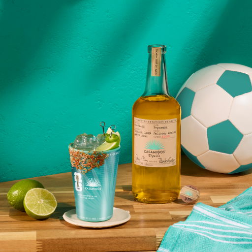 A spicy margarita with a bottle of Casamigos reposado tequila and a soccer ball on a wooden surface.