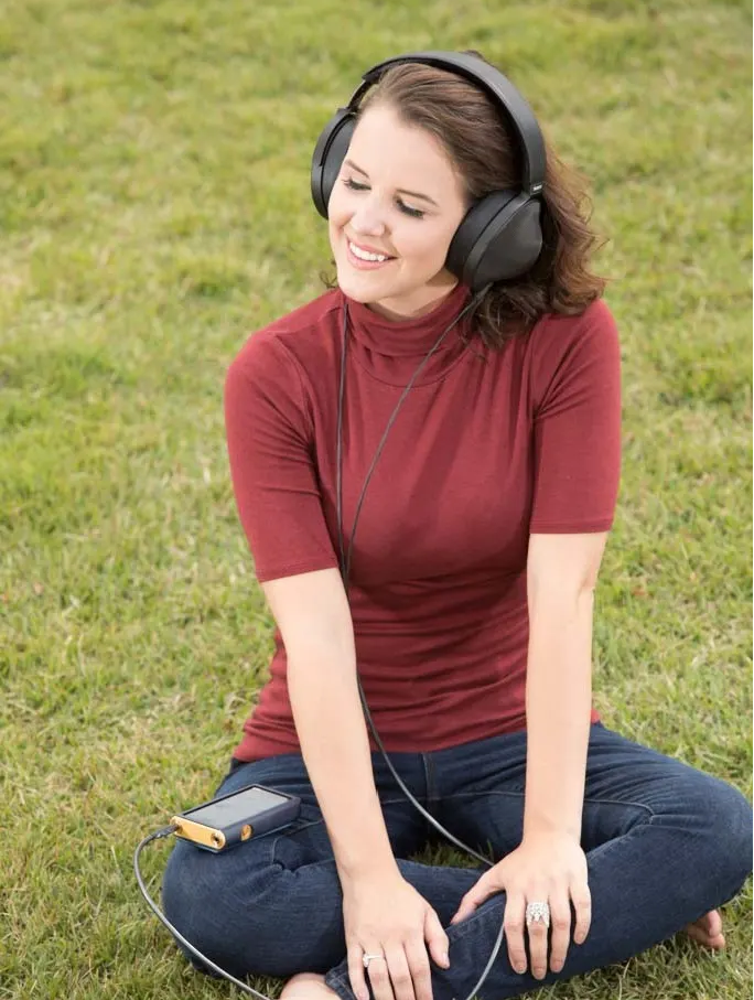 Female model sitting in the grass while listening to music with a pair of high-end full size headphone.