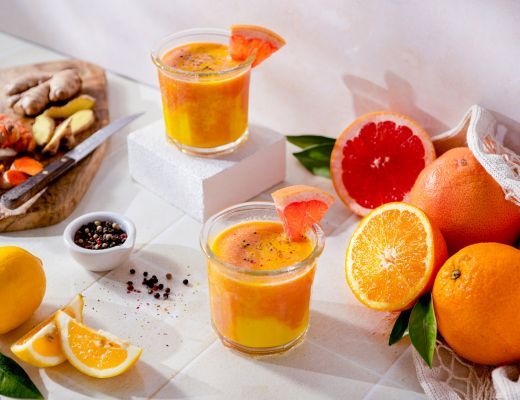 Two glasses of colorful citrus juice with fresh fruits and ginger.