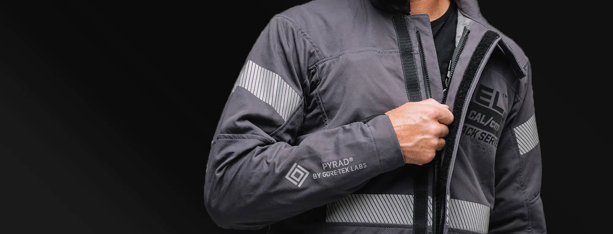 Person in a gray jacket with reflective stripes on a dark background.