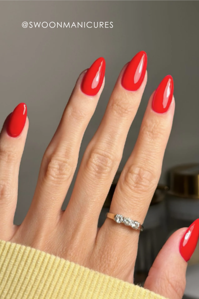 A hand with long, red nails wearing a silver ring.