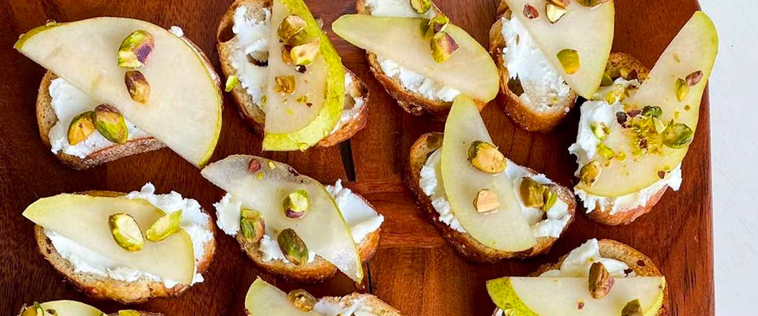 Overhead view of Crostini with Goat Cheese, Pear & Honey on a wooden platter.