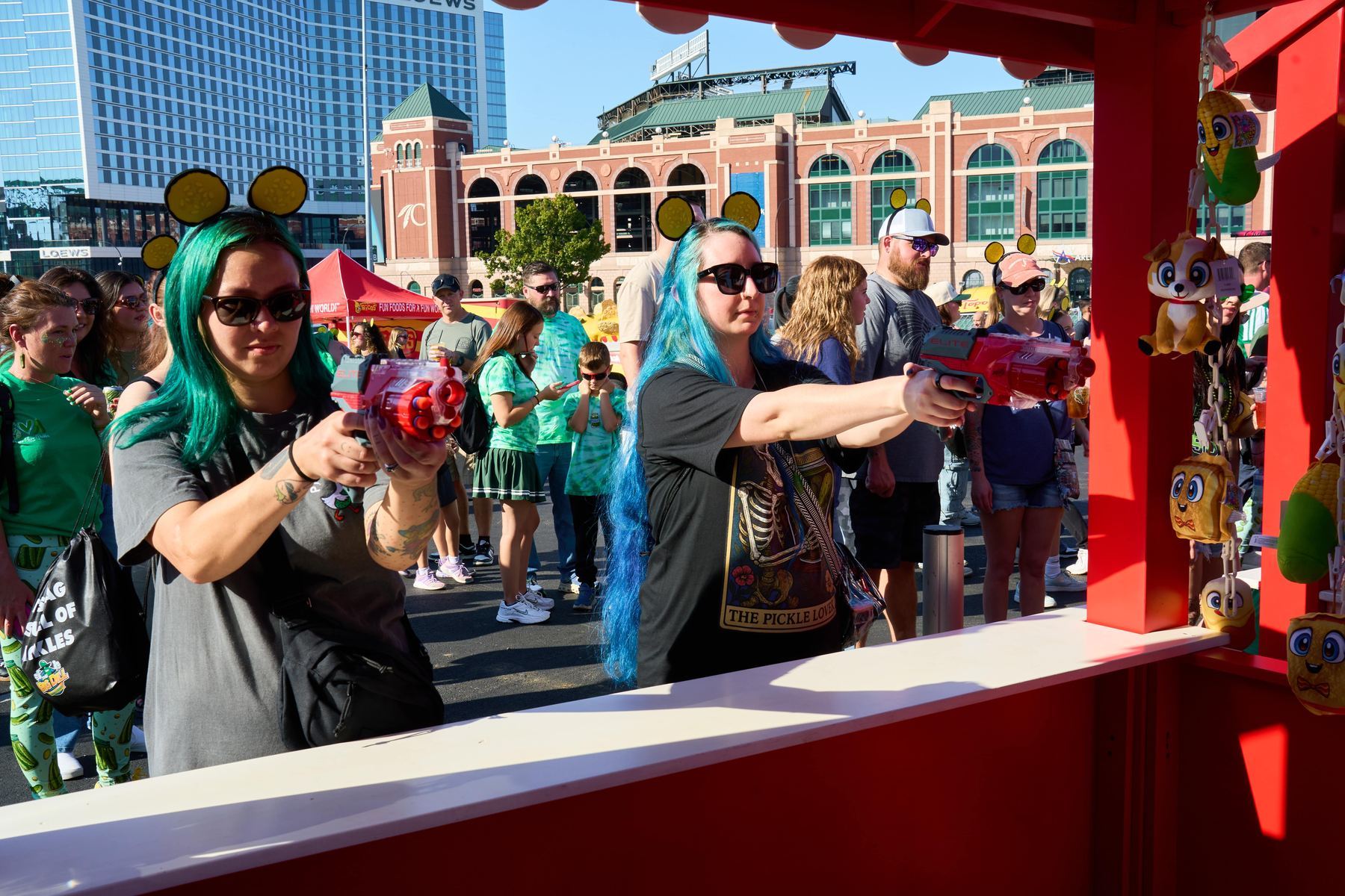Guests with green and blue wigs playing the carnival shooting game with pickle plush prizes at The Big Dill Choctaw Stadium Arlington Texas 2025.