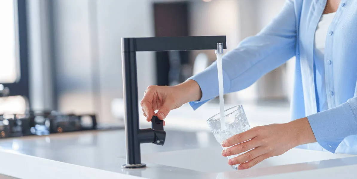 Kvinna vid kökskranen häller vatten i glas