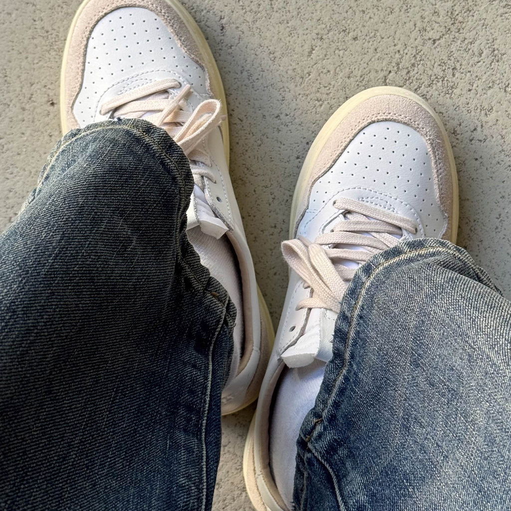 A pair of sneakers worn with blue jeans on a concrete surface.