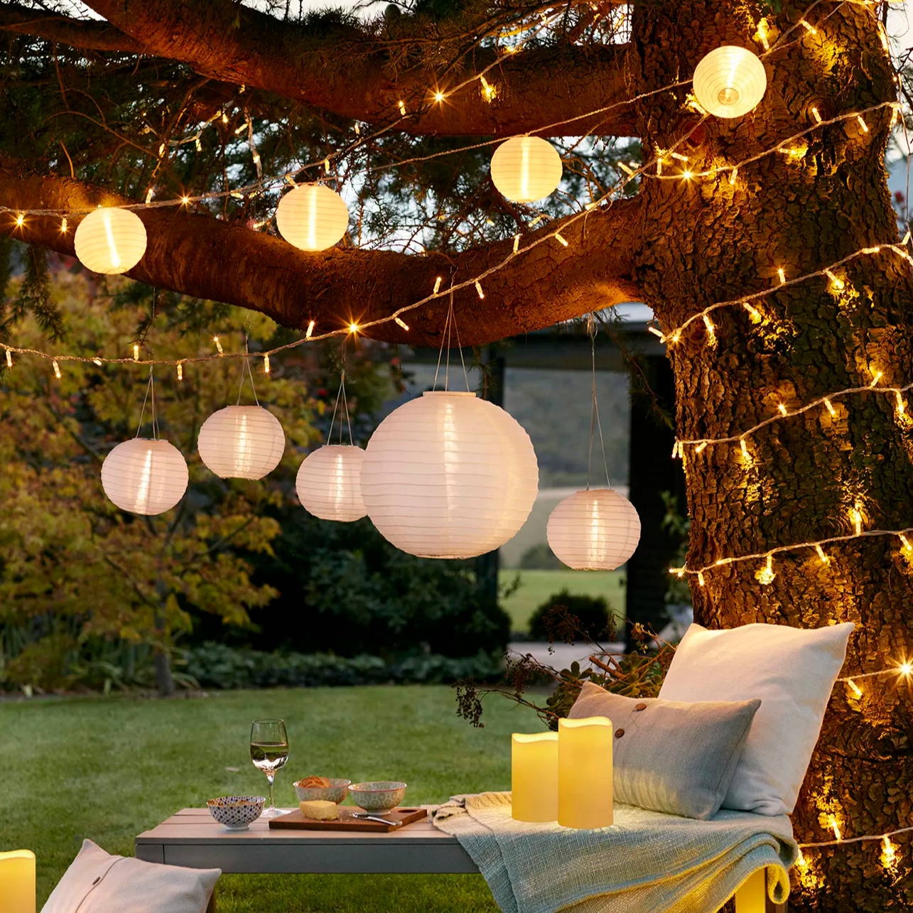 White solar lanterns and string lights hanging above an outdoor seating area with LED candles 