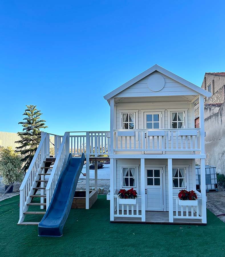 2-Story Custom Playhouse with slide, sand box and large balcony on green playground with blue sky in the back by WholeWoodPlayhouses