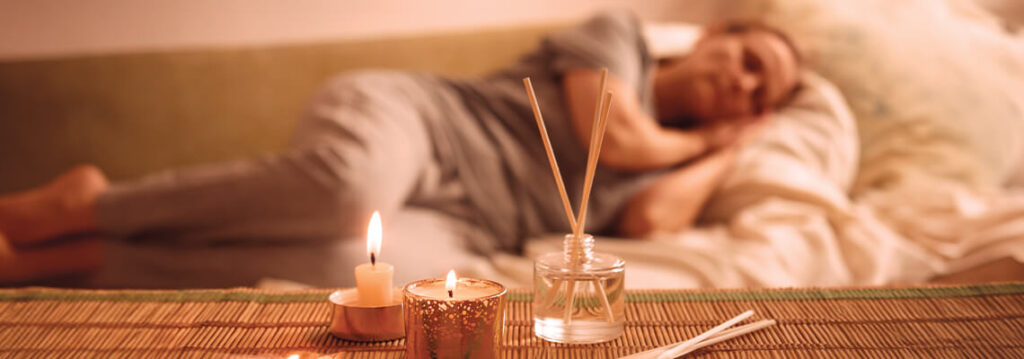 Person resting on a couch with candles and diffuser nearby.