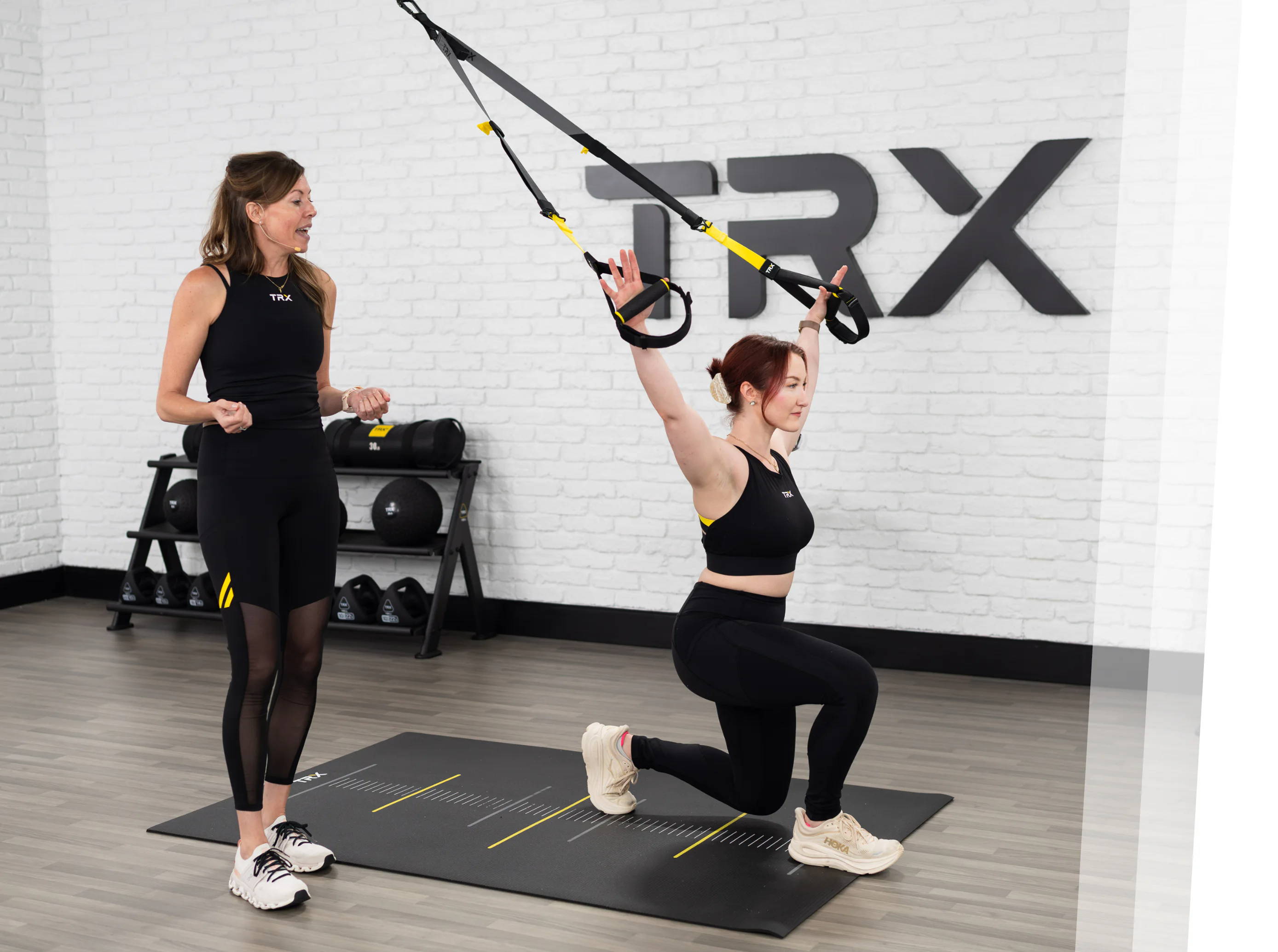 Two women exercising with TRX straps in a gym setting.