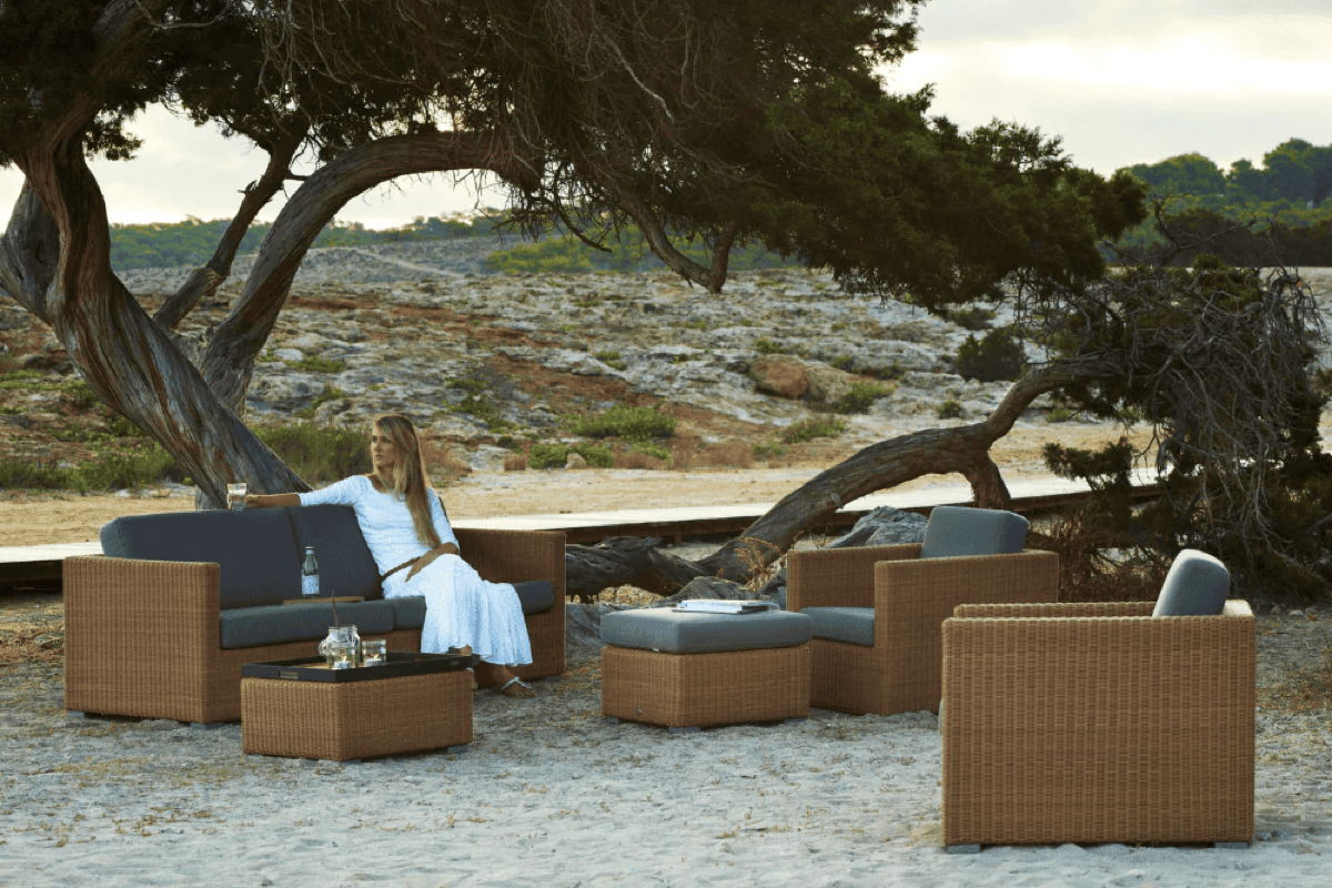 Wicker outdoor furniture set with blue cushions arranged under windswept trees, showing outdoor lounge seating in a natural coastal setting.