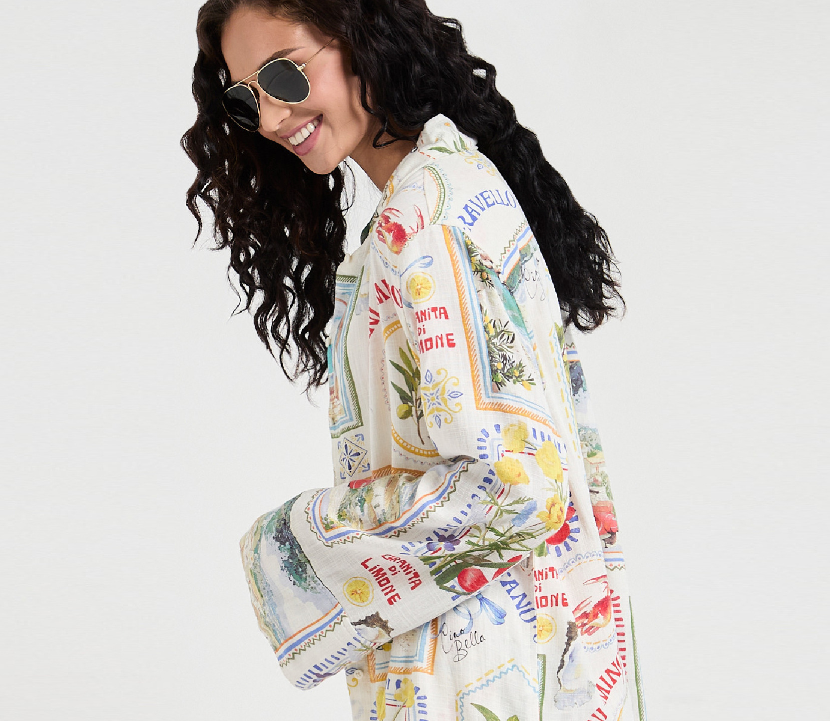 Woman with curly hair wearing sunglasses and a colorful patterned jacket.