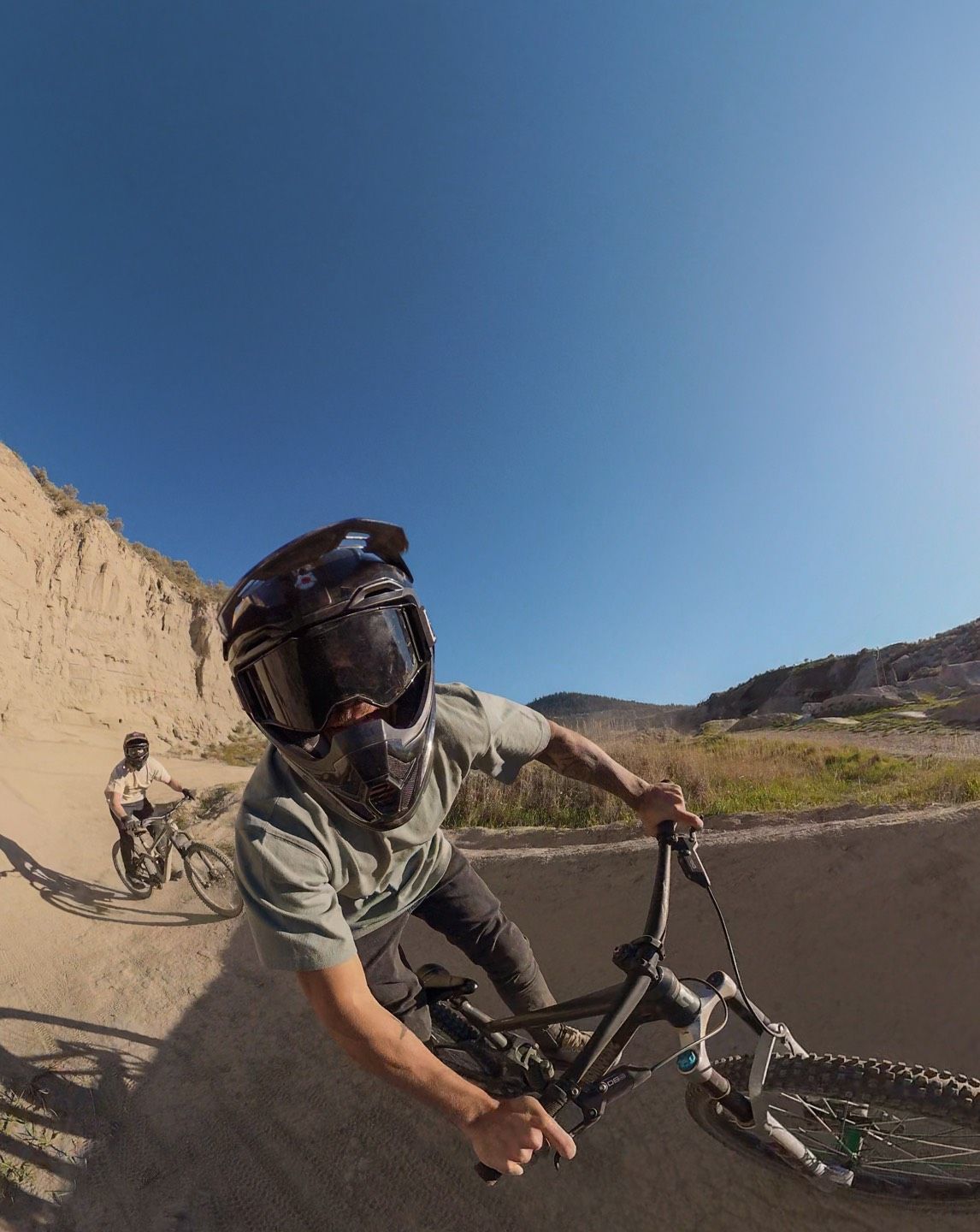 Person biking on a dirt trail with another cyclist in the background.
