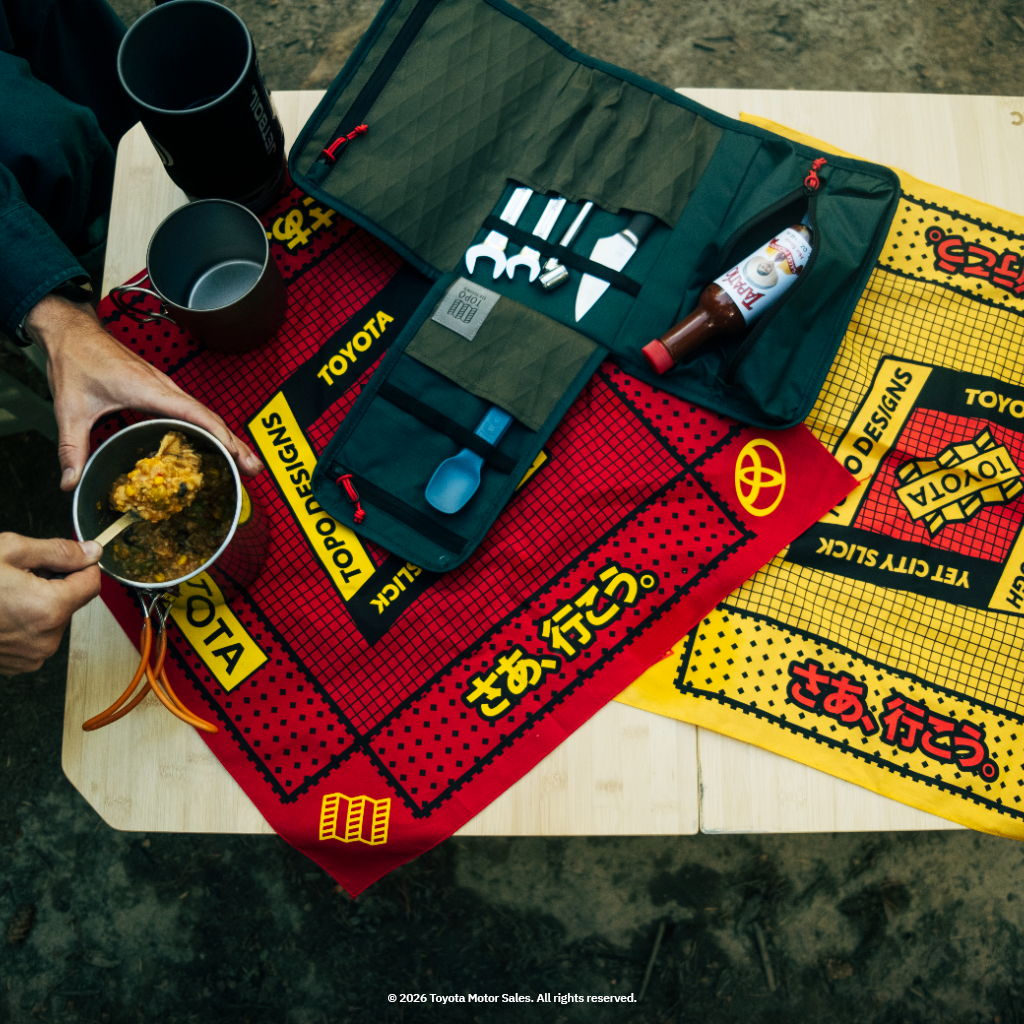 Campsite setup with colorful mats, utensils, and a bowl of food.