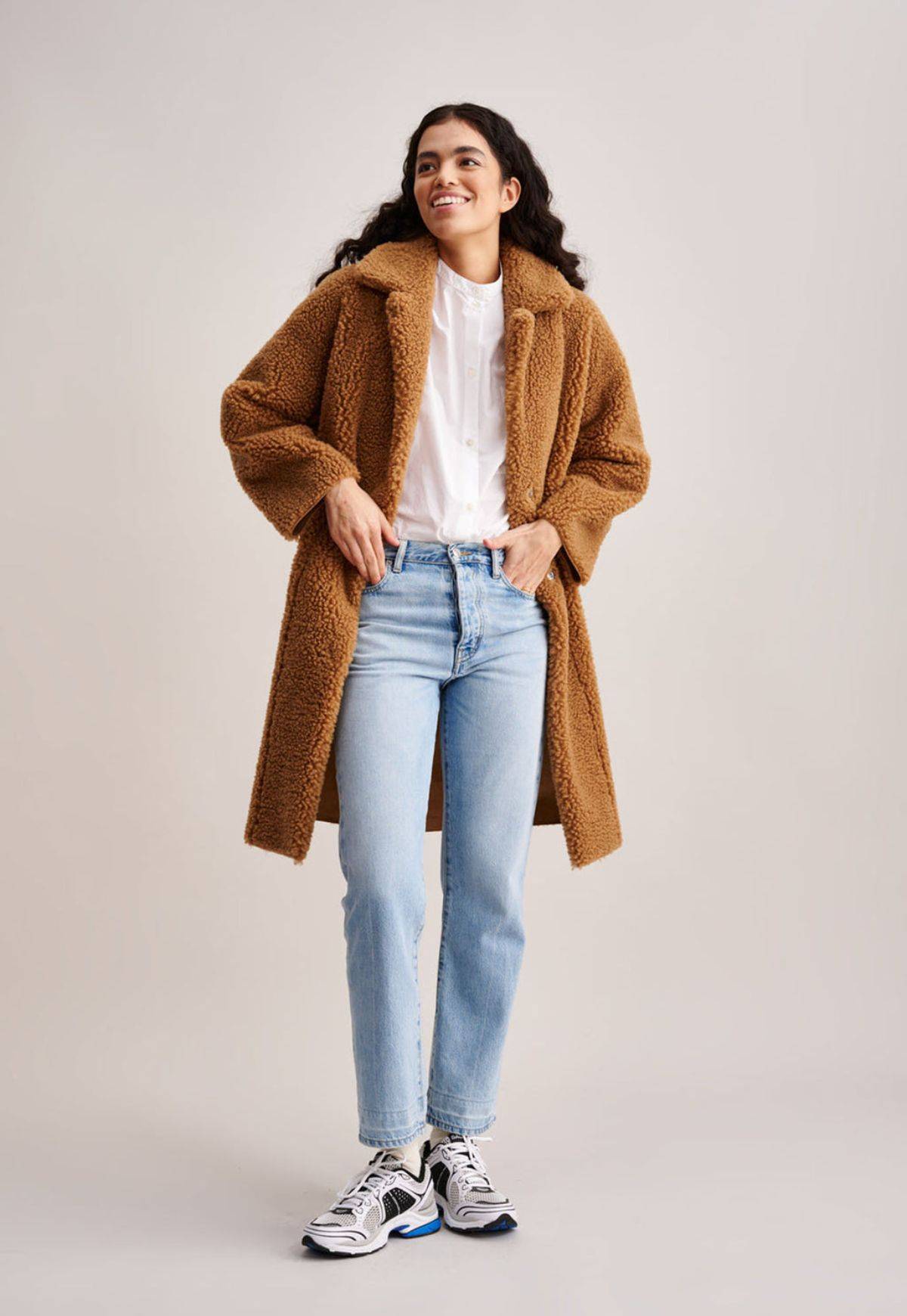 Model wearing three quarter length faux shearling fur Edith Coat in praline brown with collar.