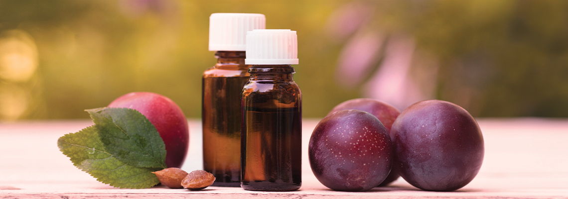Bottles of essential oil next to plums and leaves on a surface.