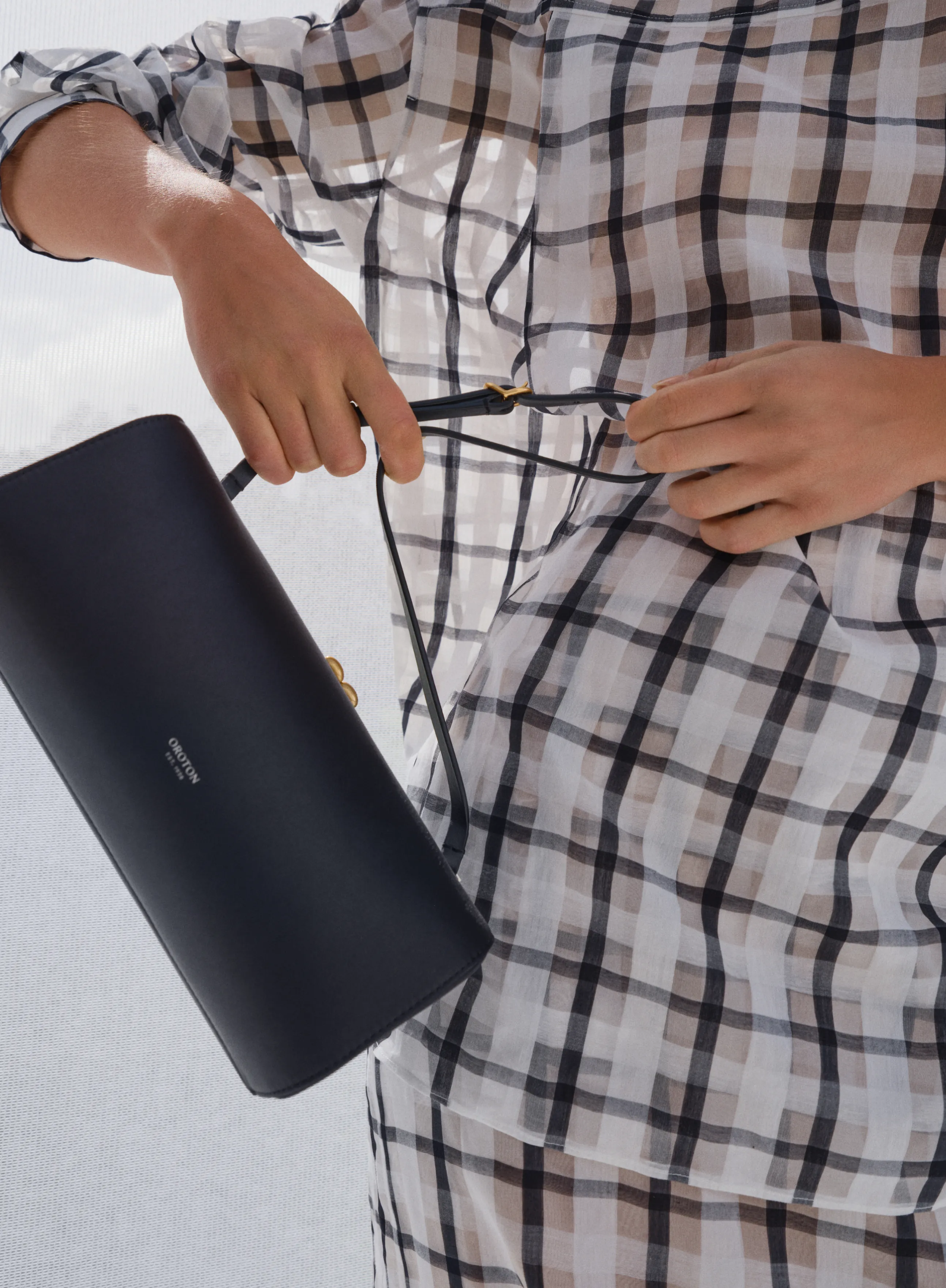 Person holding a black handbag while wearing a checkered shirt.