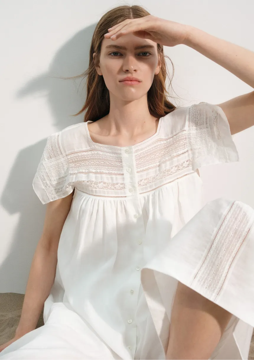 Model in a white dress, shielding eyes from sunlight.