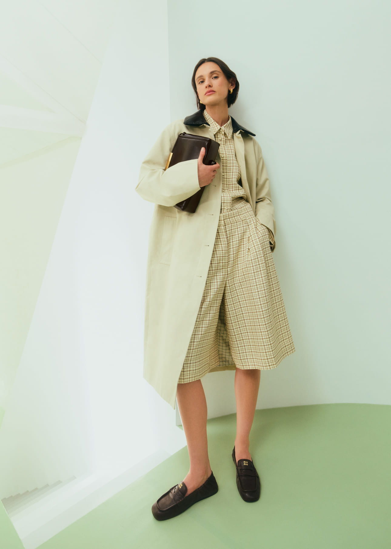 Woman in fashionable coat and shorts, standing against a minimalist background.