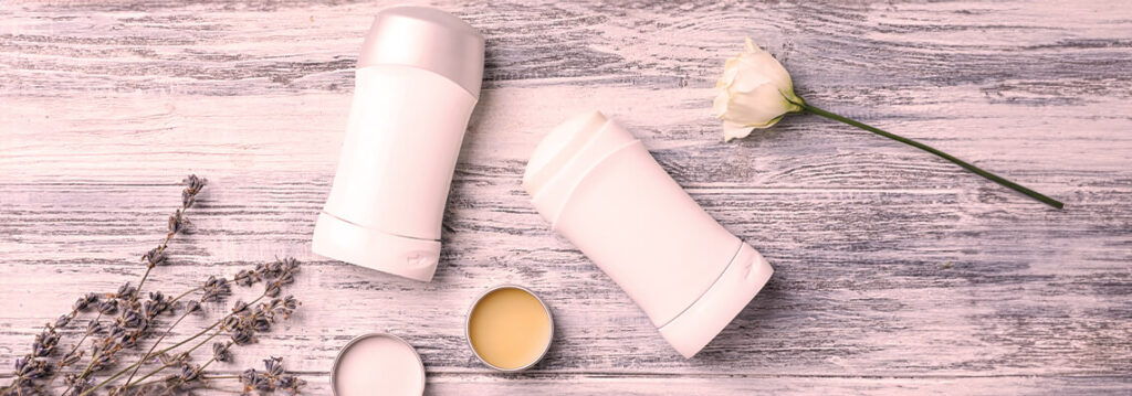 Two cosmetic containers and a flower on a wooden surface.