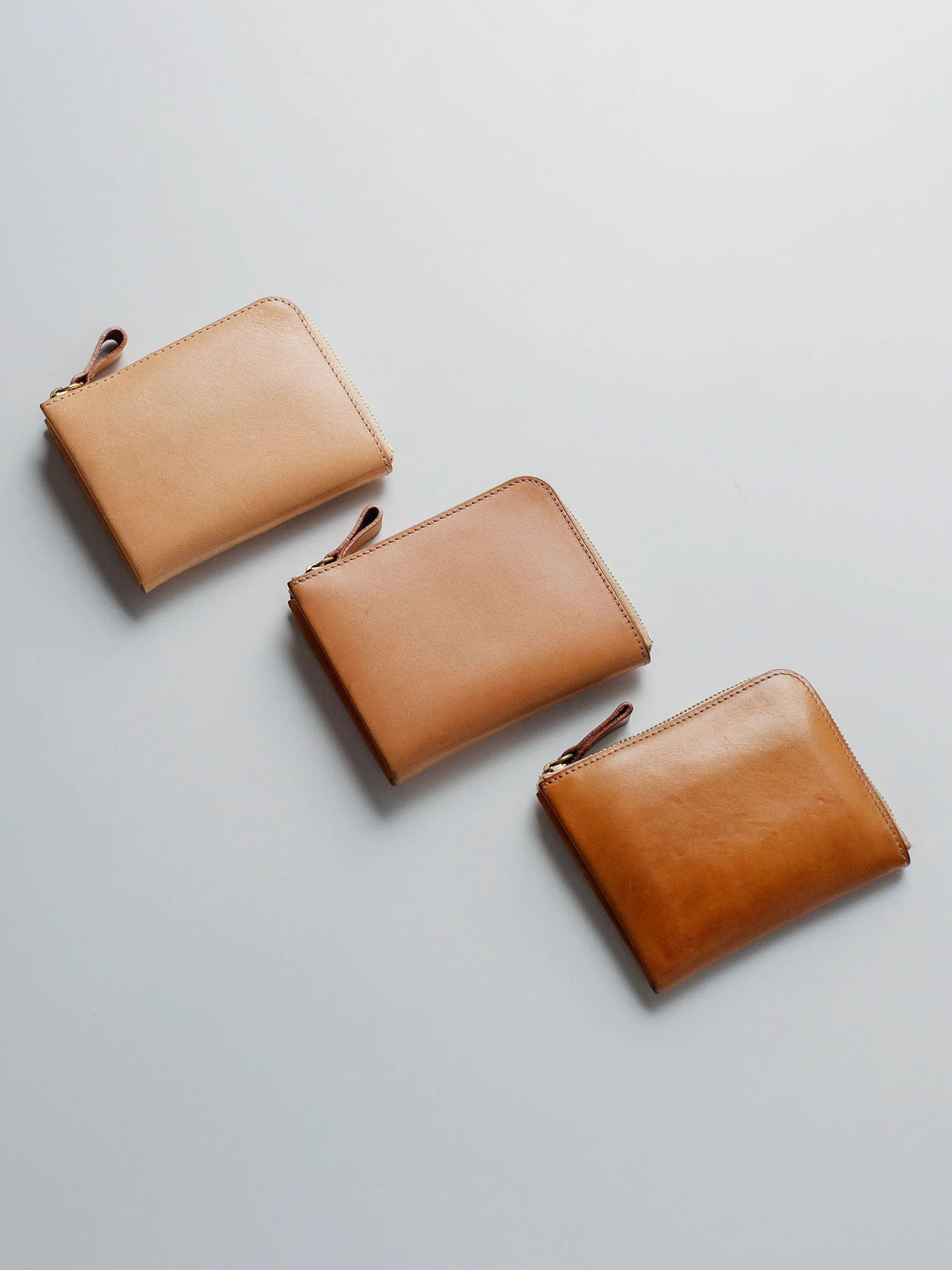 Three brown leather wallets arranged in a row on a light background.